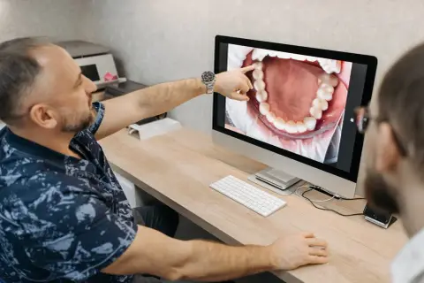 Dentysta pokazuje pacjentowi na monitorze zdjęcie jamy ustnej, wskazując na problem, jak boli kieszonka dziąsłowa.