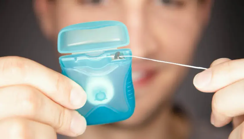 Mężczyzna trzyma niebieskie opakowanie z nicią dentystyczną (floss).