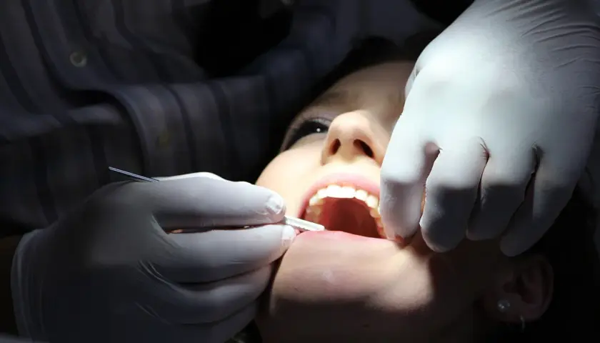 Dentysta w białej rękawiczce wykonuje zabieg zatruwania zęba u pacjentki.