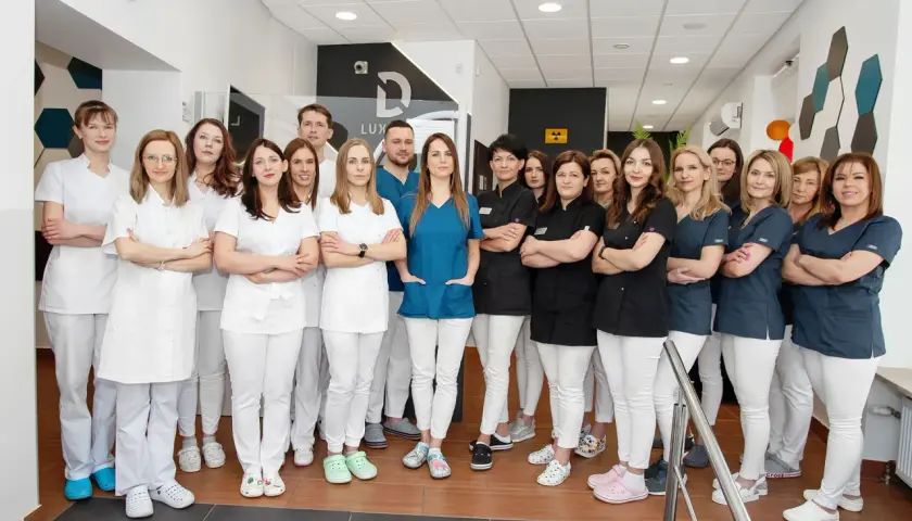 Grupa uśmiechniętych dentystów w białych i granatowych uniformach stoi w gabinecie.