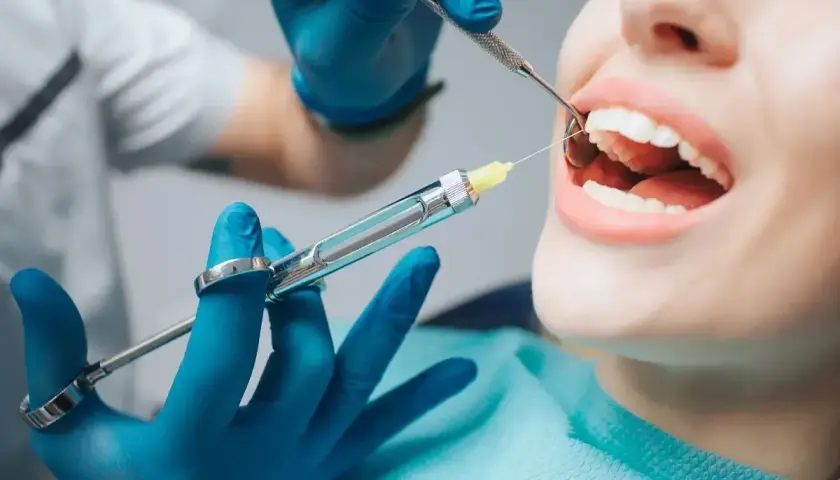 Dentysta wykonuje znieczulenie przewodowe, podając środek znieczulający do jamy ustnej pacjenta.