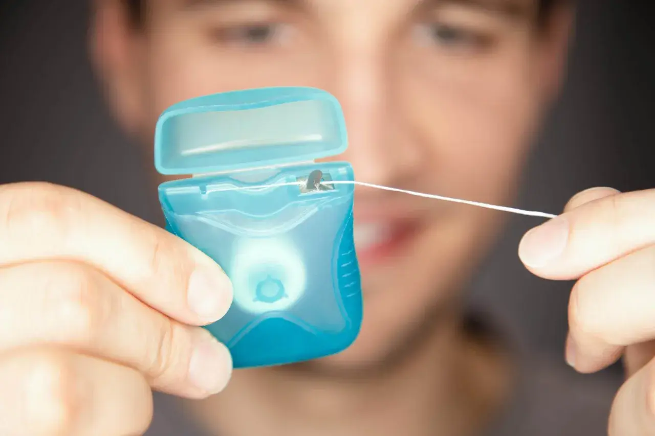 Mężczyzna trzyma niebieskie opakowanie z nicią dentystyczną (floss).